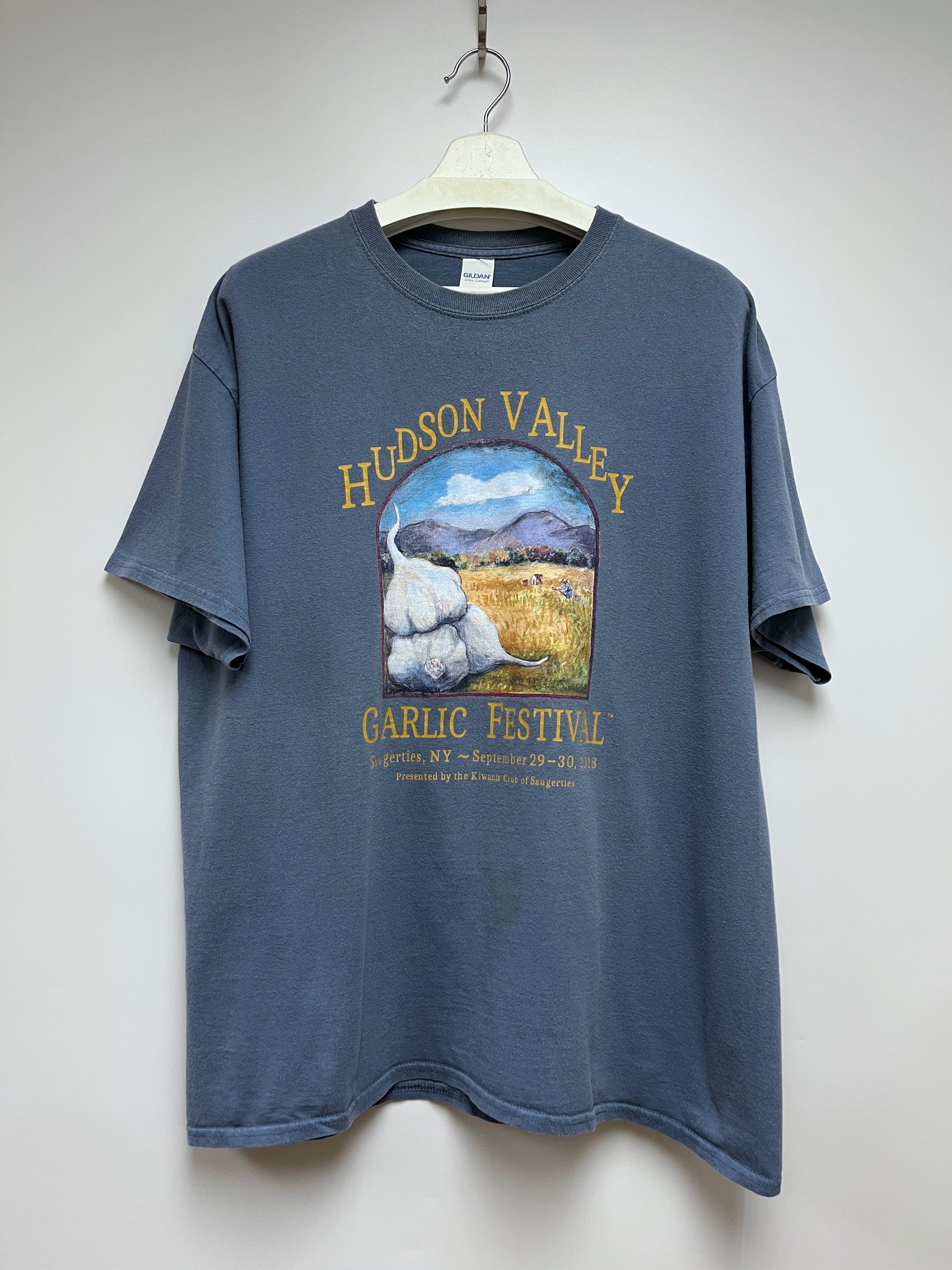 Blue t-shirt with Hudson Valley Garlic Festival graphic on a white hanger against a white background