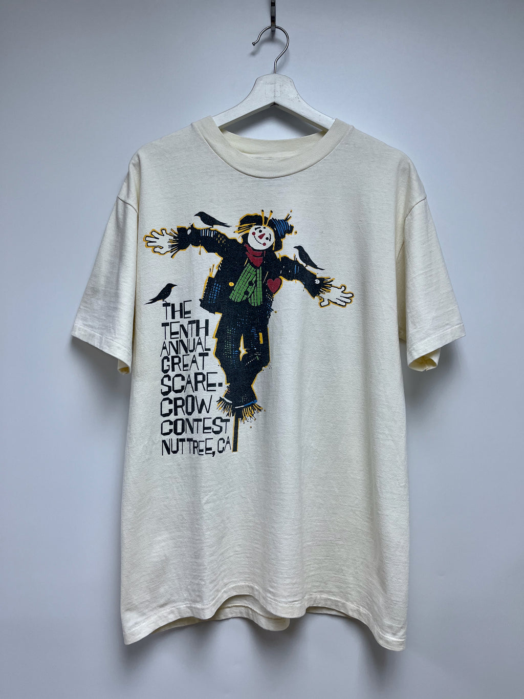 Beige t-shirt with scarecrow graphic and text on a white background