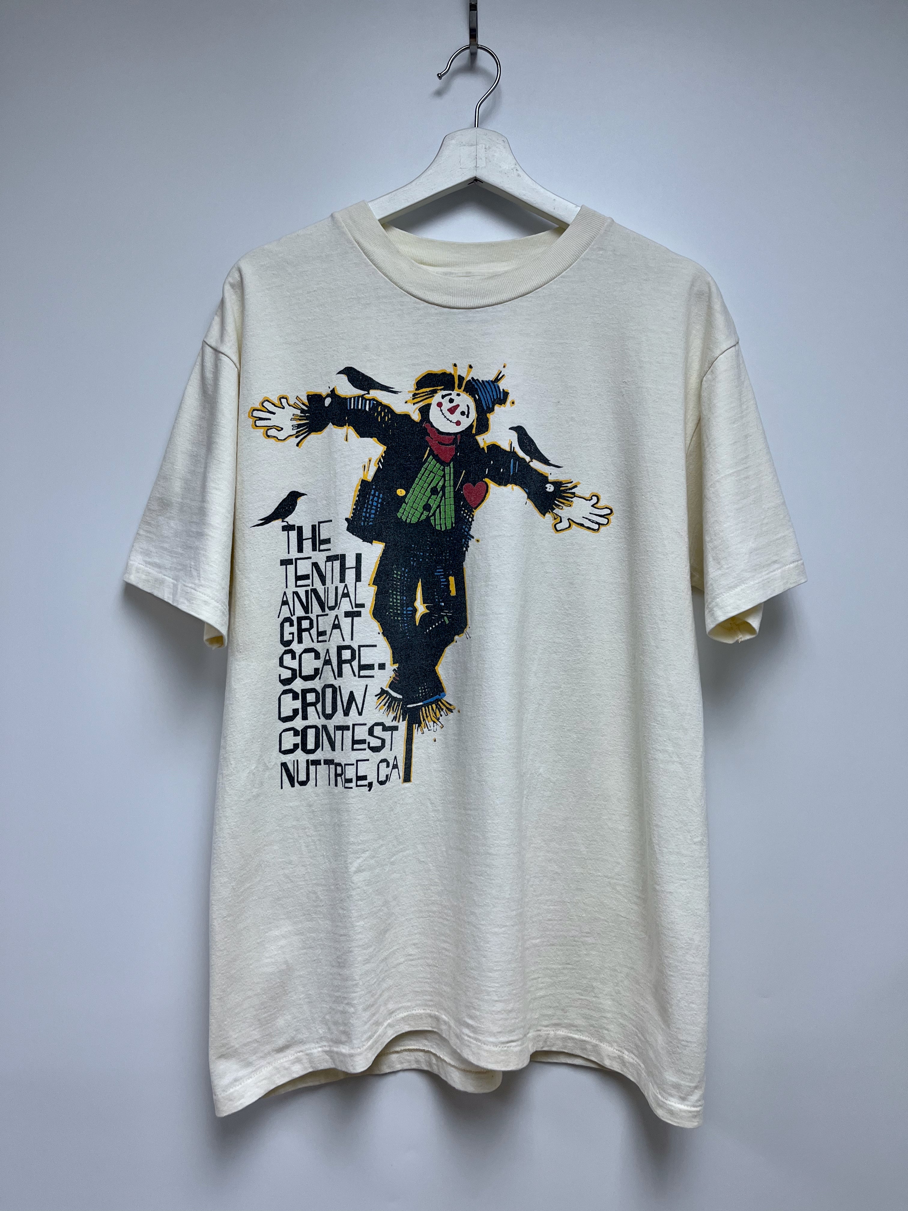 Beige t-shirt with scarecrow graphic and text on a white background