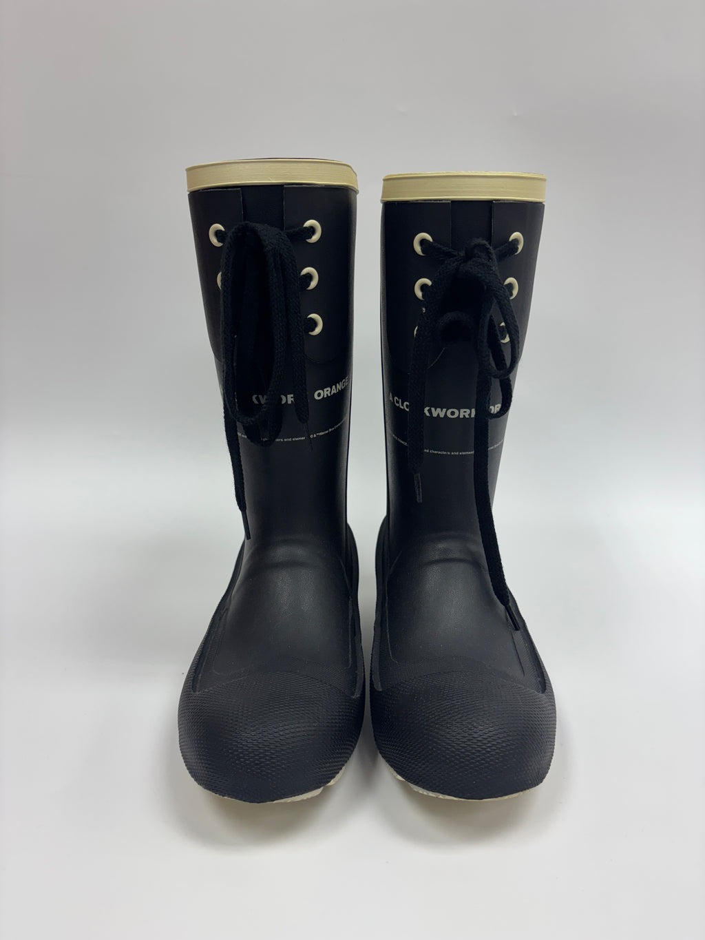A pair of black rubber work boots with beige trim at the top and beige soles, featuring black laces and white text reading 'DLC WORK' on the sides, photographed against a light gray background.