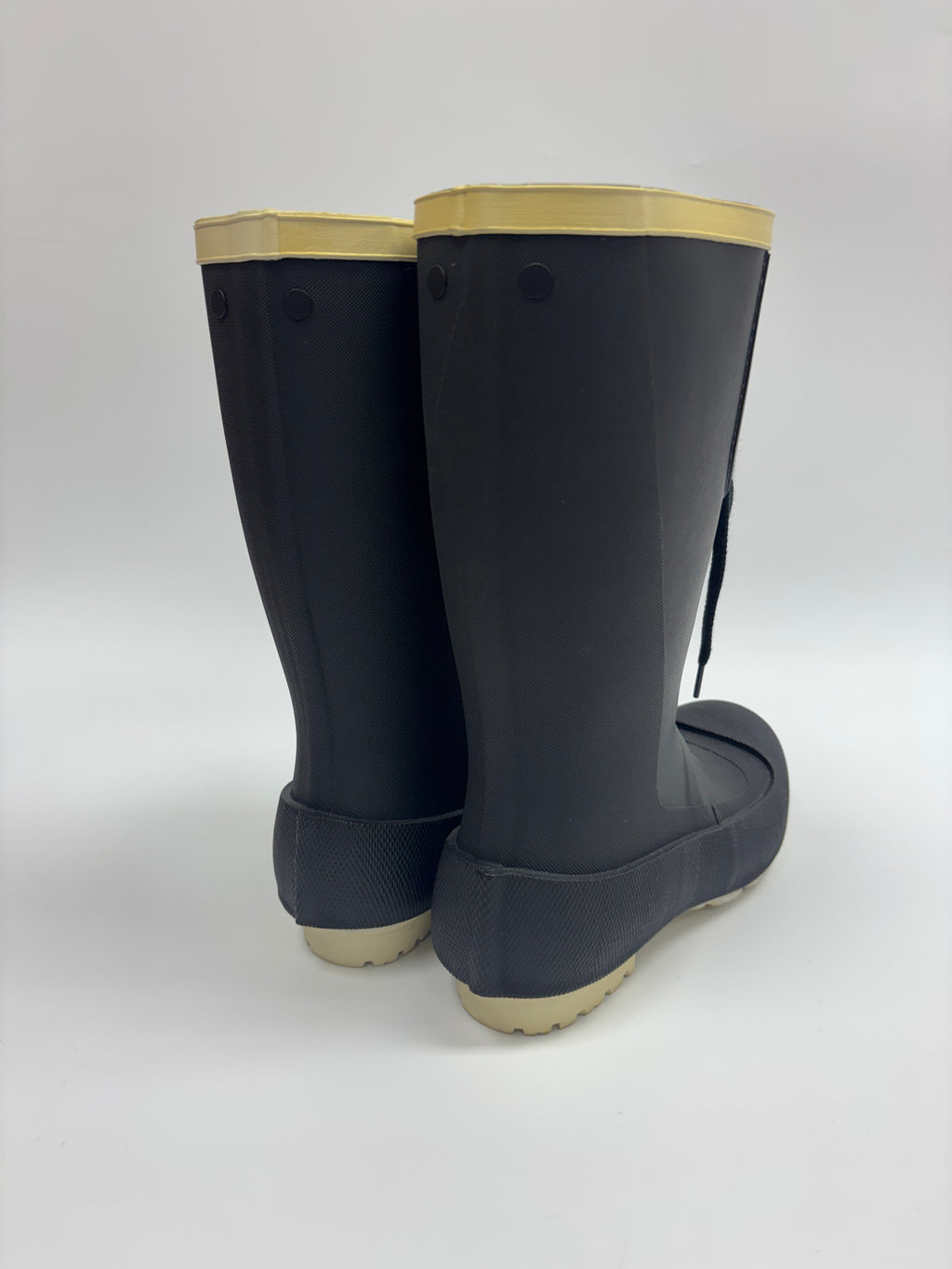 A pair of dark gray rubber rain boots with light beige soles and collar trim, shown from a rear three-quarter angle on a light gray background.