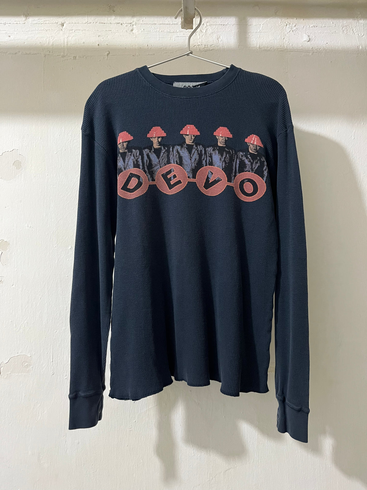 NAVY THERMAL long-sleeve shirt with graphic design and 'DEVO' text on a white wall.