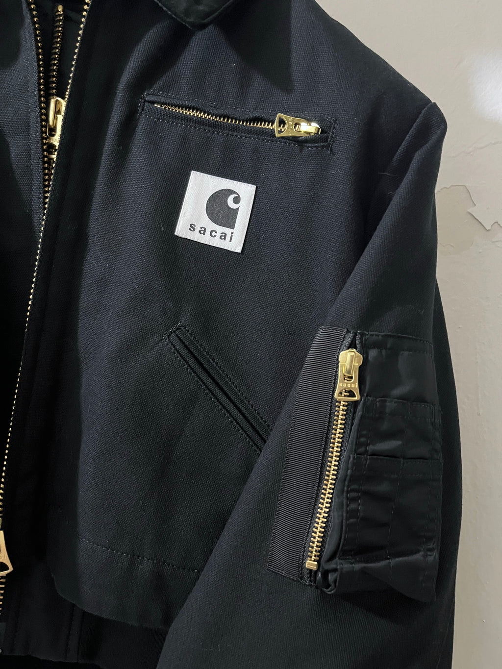 Black jacket with gold zippers and a visible brand logo on a neutral background